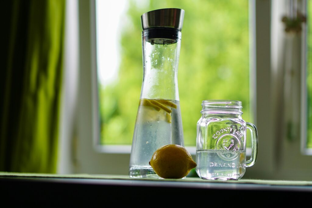 Home Lemon-infused water in a glass carafe and mason jar on a windowsill, evoking freshness.