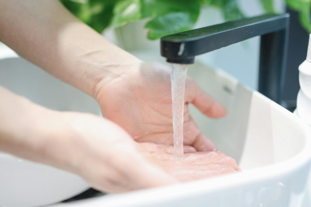 Home Hands washing under a modern bathroom faucet, emphasizing hygiene and cleanliness.