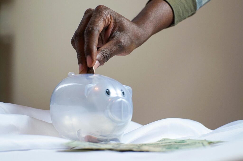 Home Close-up of a person's hand placing coins into a transparent piggy bank to save money.